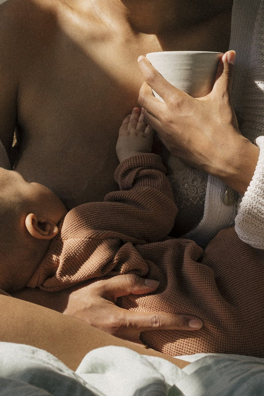 Une maman qui allaite et tient son bébé dans les bras tout en dégustant une tasse de la poudre collagène Mamalaod de Jolly Mama