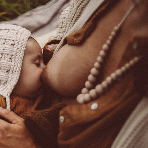 Maman donnant le sein à son bébé endormi et ayant autour du cou le Jolly collier d'allaitement, de dentition et de portage de Jolly mama