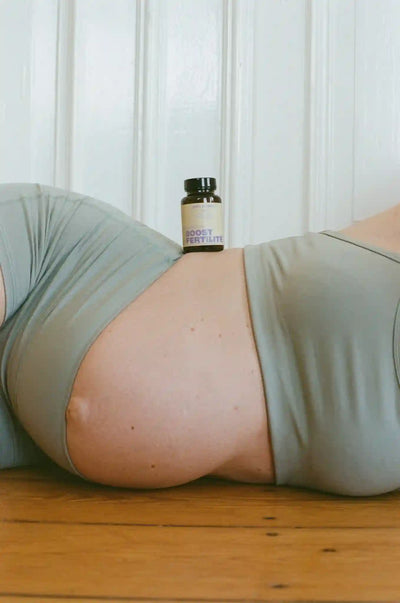 Femme enceinte allongée sur le côté avec un flacon OVO + Boost Fertilité posé sur son ventre.