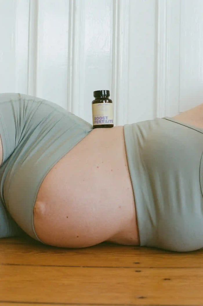 Femme enceinte allongée sur le côté avec un flacon OVO + Boost Fertilité posé sur son ventre.