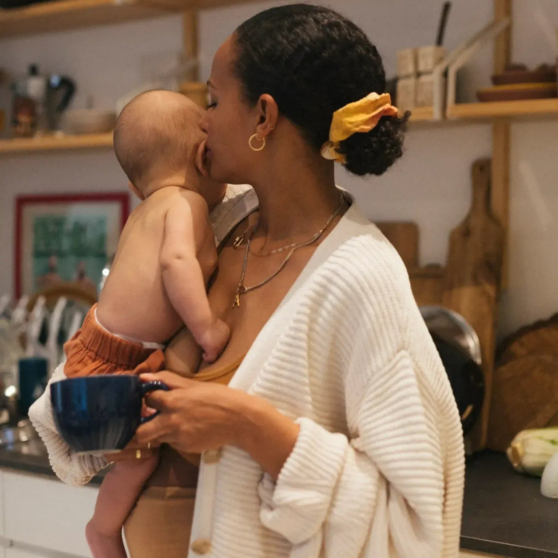 Maman qui savoure une boisson tout en portant son bébé dans sa cuisine