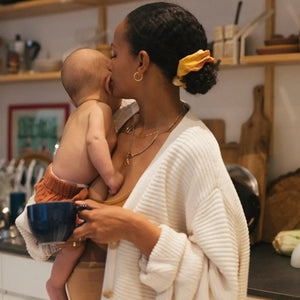 Maman qui savoure une boisson tout en portant son bébé dans sa cuisine