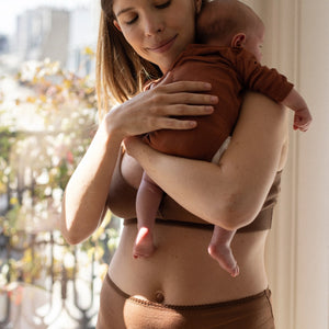 Maman en post-partum tenant son nouveau-né, moment de douceur à la maison.