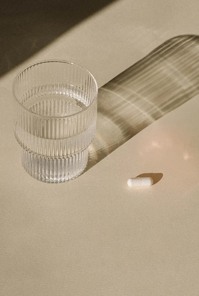 Complément alimentaire en capsule blanche posé à côté d’un verre d’eau sur fond lumineux – magnésium naturel pour la détente et la récupération.