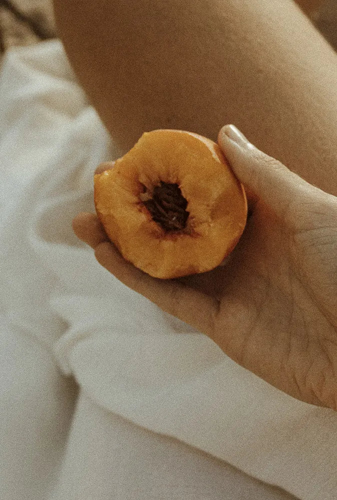 Main féminine tenant une demi-pêche, en ambiance douce et naturelle – symbole de vitalité et de bien-être au féminin, idéal pour illustrer un complément naturel pour la ménopause.