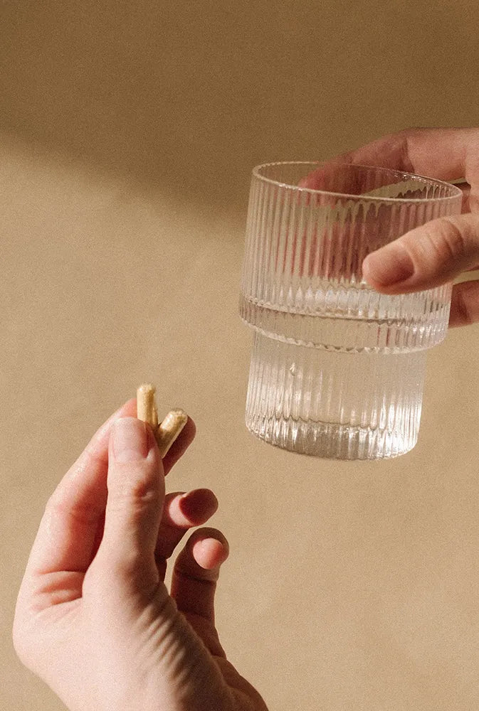 Main tenant des gélules végétales accompagnée d’un verre d’eau, sur fond neutre – complément alimentaire pour combler les carences en vitamines et minéraux chez la femme.