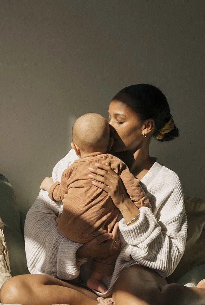 Jeune maman embrassant tendrement son bébé, image chaleureuse et naturelle illustrant la douceur de la maternité et l'importance des compléments contre la fatigue post-partum.