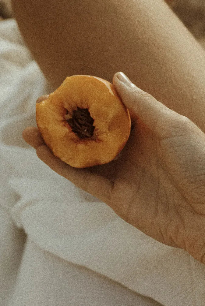 Main féminine tenant une demi-pêche, en ambiance douce et naturelle – représentation symbolique du cycle féminin et du soulagement naturel des symptômes liés au syndrome prémenstruel (SPM).