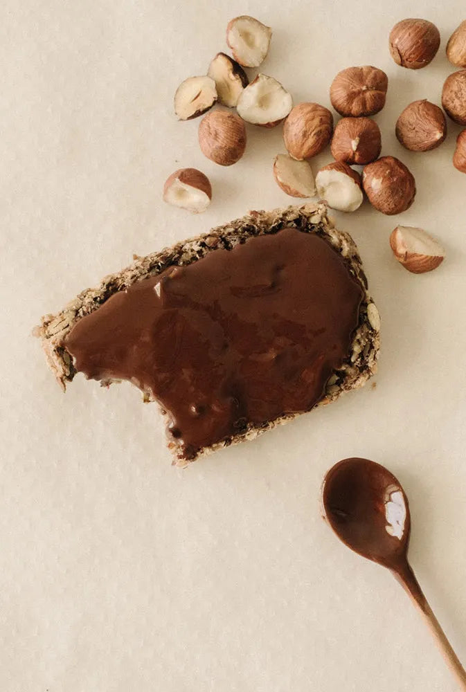 Tartine croquante nappée de pâte à tartiner chocolat-noisette Jolly Mama, accompagnée de noisettes entières – encas sain et gourmand pour les mamans et futures mamans.