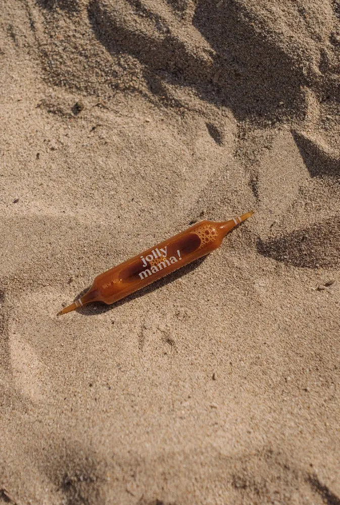 Ampoule de complément alimentaire Light legs posée sur le sable – solution naturelle estivale pour soulager les jambes lourdes des futures et jeunes mamans en vacances.