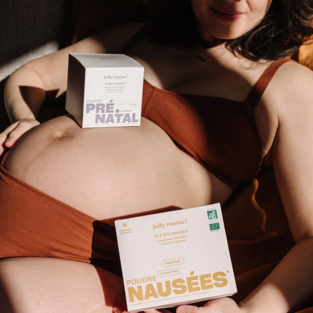 Femme enceinte avec deux boîtes posées sur son ventre : Bump Essentials, le multivitamines grossesse en poudre, et Bye Bye Nausea, le complément anti-nausées.