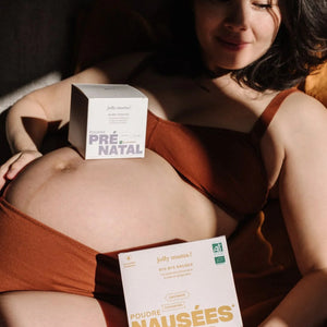 Femme enceinte allongée, tenant la Poudre Prénatale Baby Bump et la Poudre Nausées Bye bye nausea de Jolly Mama – compléments bio pour soutenir la grossesse