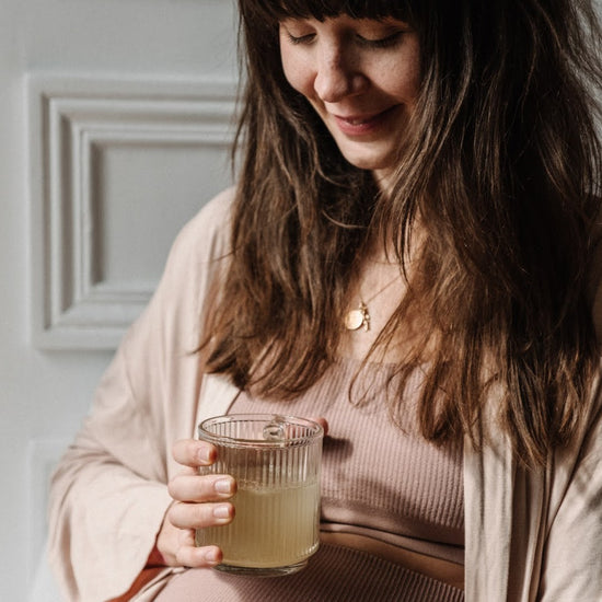 Femme enceinte avec le verre de Bye Bye Nausea posé sur son ventre et souriant