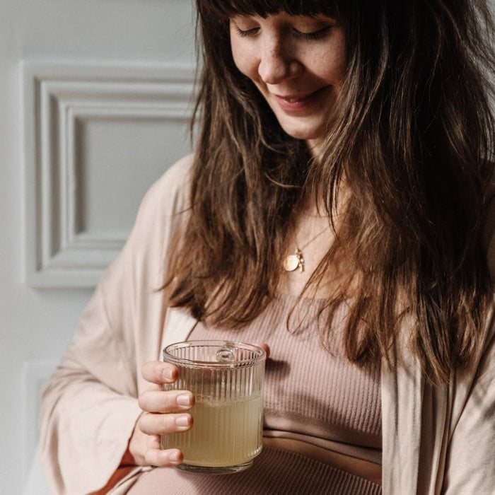 Femme enceinte avec le verre de Bye Bye Nausea posé sur son ventre et souriant