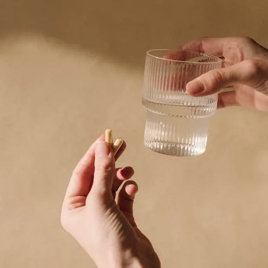 verre d'eau avec 2 gélules dans la main