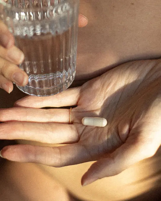gélule dans une main avec verre d'eau