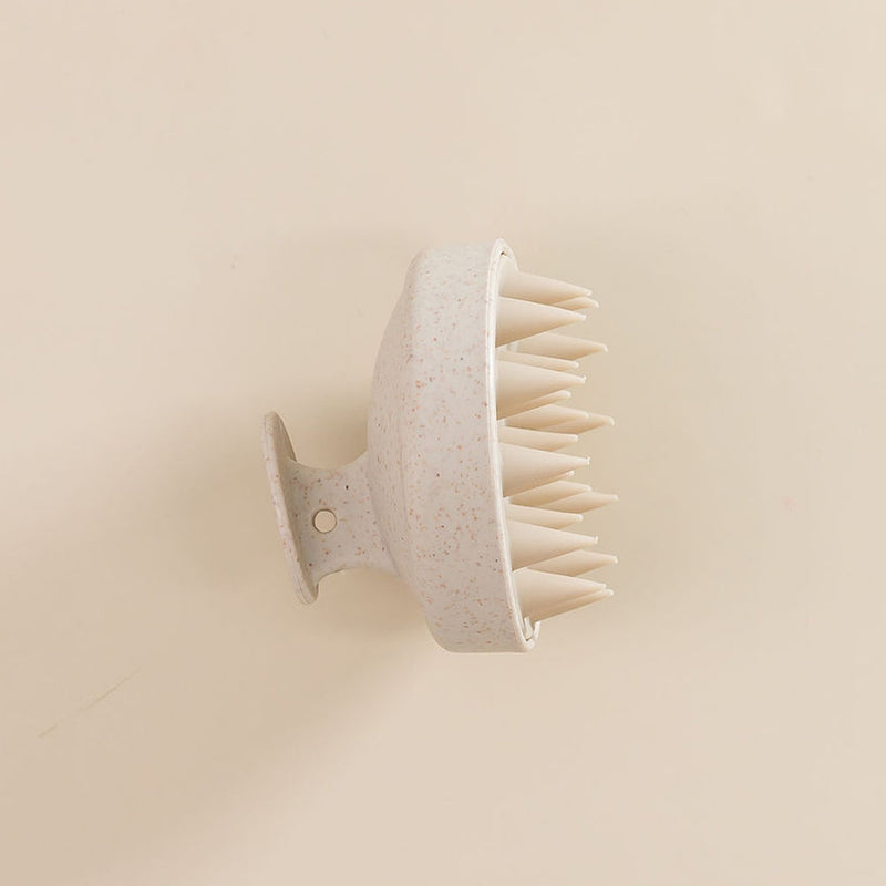 Brosse en silicone pour cuir chevelu, vue de côté, posée sur une surface. 

