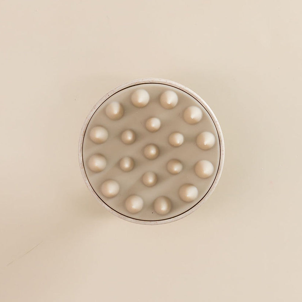 Brosse avec des picots en silicone pour cuir chevelu, vue de dessus, posée sur une surface.







