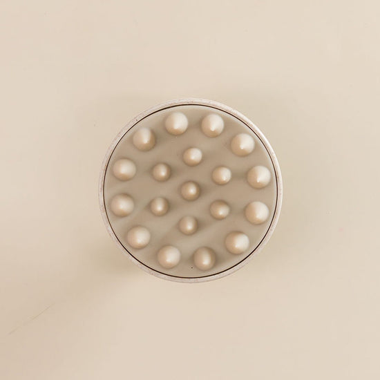 Brosse avec des picots en silicone pour cuir chevelu, vue de dessus, posée sur une surface.







